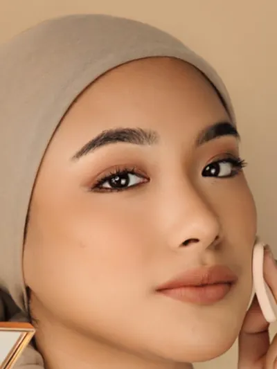 Model berhijab berkulit kuning langsat menepuk pipi dengan spons, shade Neutral