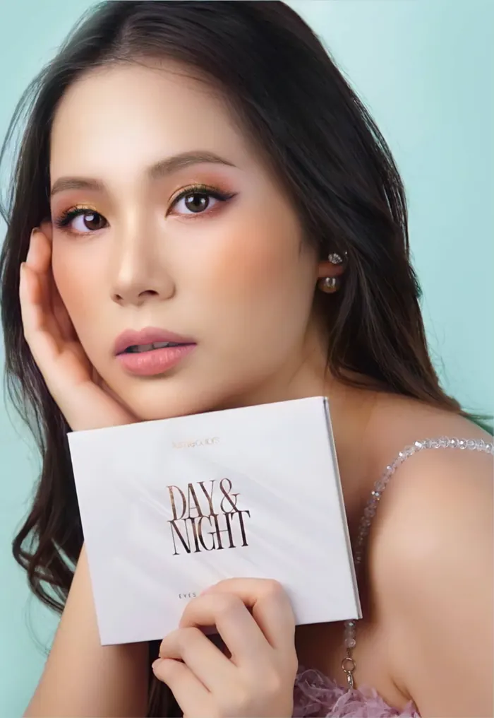 Model berambut panjang bergelombang dengan eyeshadow bronze memegang kotak Day & Night