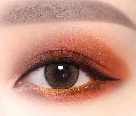 Mata dengan eyeshadow oranye karat smokey, garis emas di bawah dan eyeliner bersayap