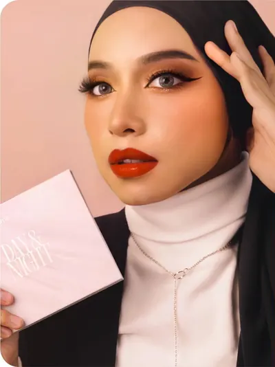 Model berhijab hitam dengan bibir oranye-merah memegang kotak Day & Night
