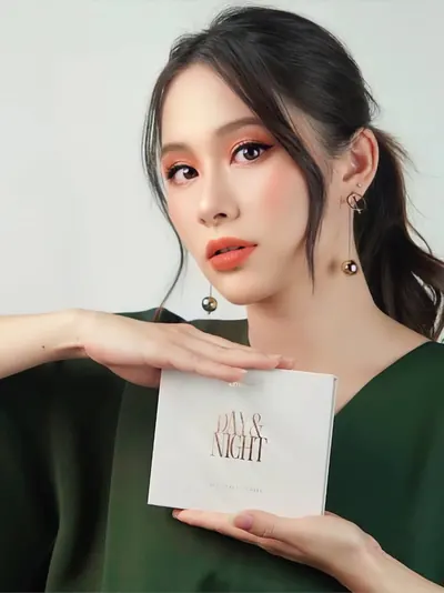 Model berambut gelap dengan atasan hijau memegang kotak Day & Night