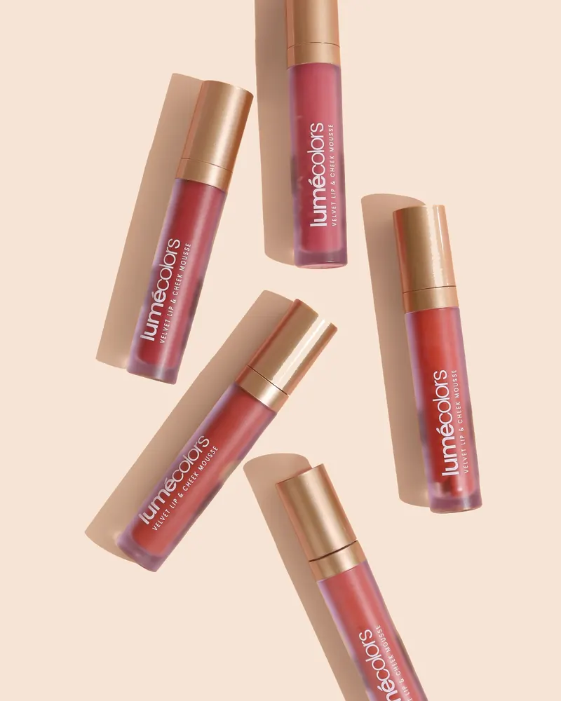 Tube Lumécolors Velvet Lip & Cheek Mousse dalam aneka warna di atas latar peach