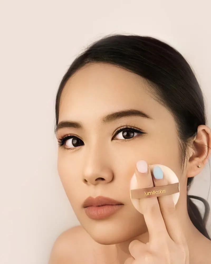 Model menepuk bedak ke pipi dengan puff Lumécolors