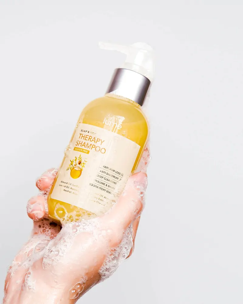 Tangan berbusa memegang botol Lume Scalp & Hair Therapy Shampoo